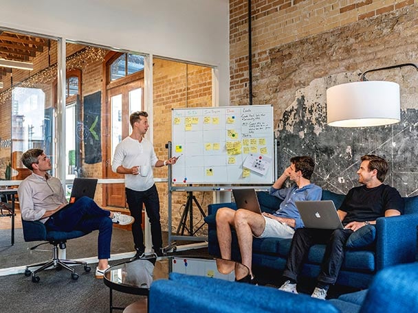 Vier Mitarbeitende in einem Sitzungszimmer vor einer beschriebenen Tafel