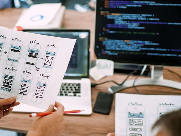 Zweo Mitarbeitende, die mit handgeschriebenen Notizen an einem PC arbeiten