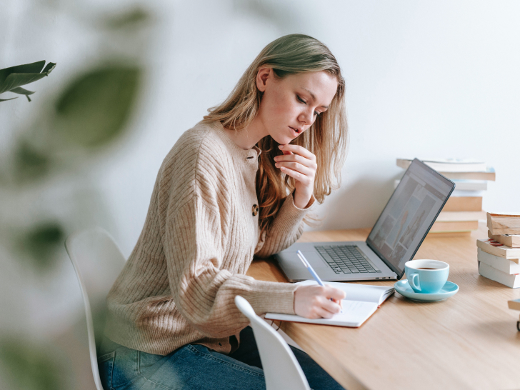 woman working on a laptop and making notes in a notebook