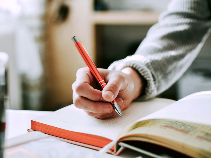 Hand, die einen Stift hält, der Notizen in einem Buch macht