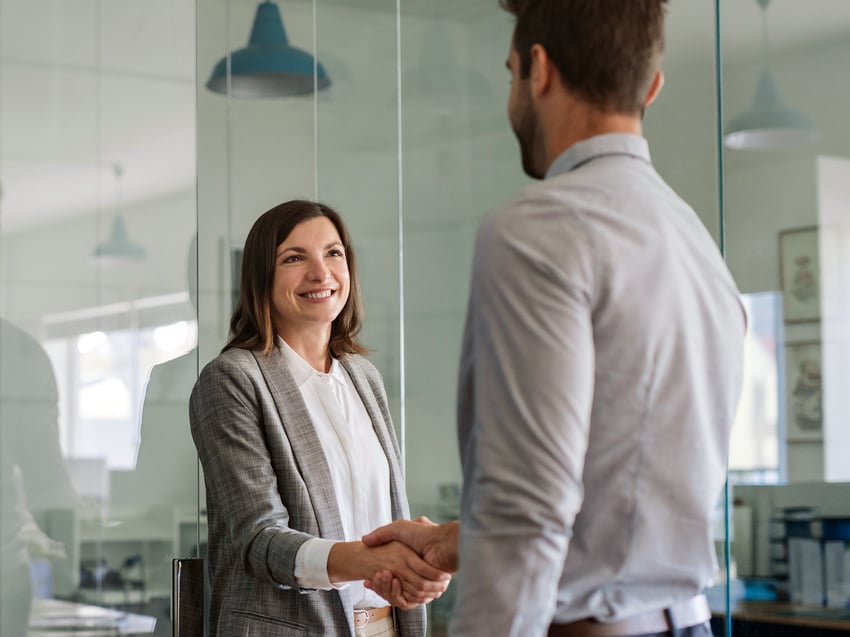 Female colleague seen from front shaking hand of male colleague seen from back 