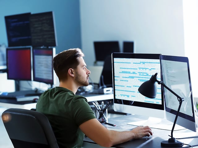 Man sitting in an office looking at two screens