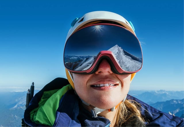 Women staring at a snow covered mountain range reflected in her goggles
