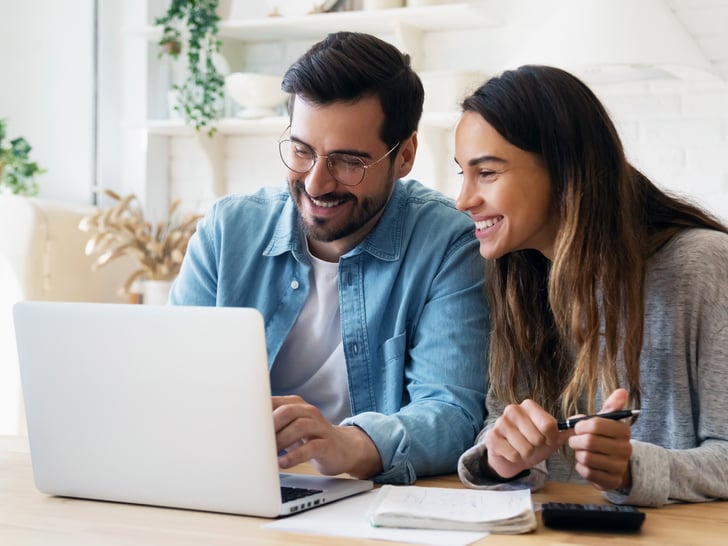 Weibliche und männliche Arbeitskollegen schauen lächelnd auf denselben Laptop-Bildschirm 