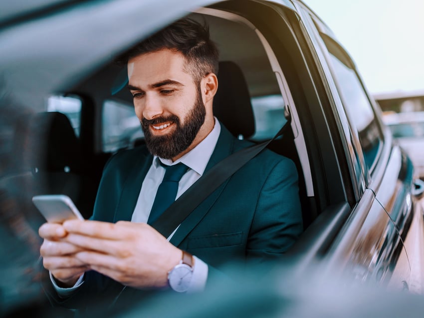 Mann in Anzug sitzt in Auto und schaut auf sein Smartphone 