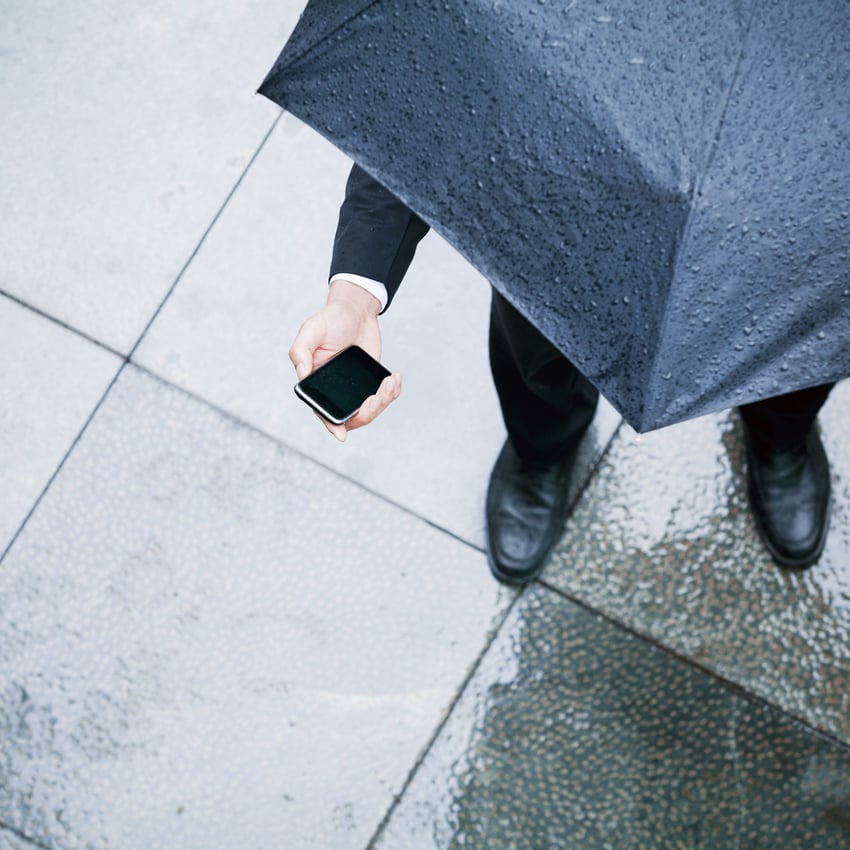 Businessman under umbrella holding smartphone seen from bird’s eye perspective 