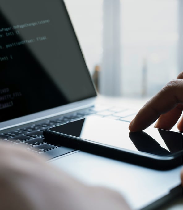 Hand touching smartphone lying on laptop keyboard 