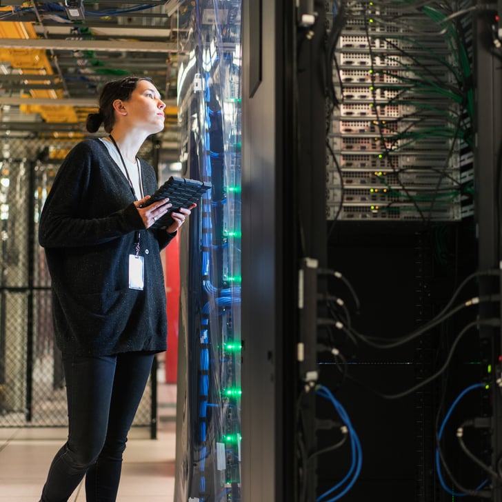 Woman in server room looks at cables behind glass 