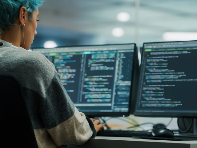 Woman looking at two computer screens with code 