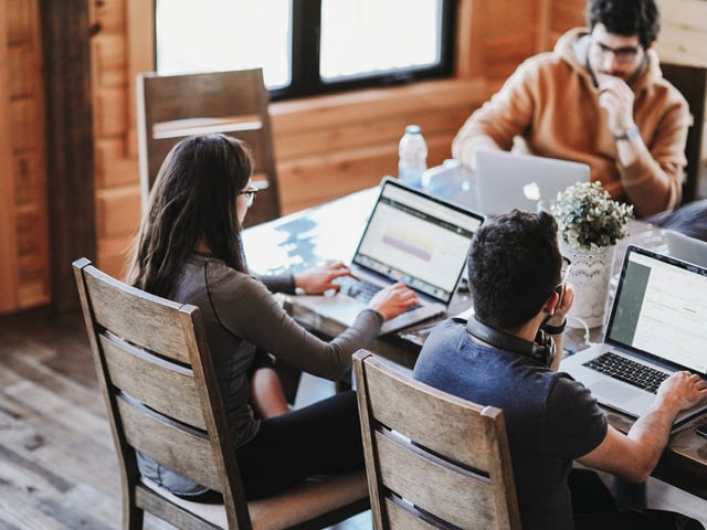 Zwei männliche und eine weibliche Kollegin sitzen am Schreibtisch und arbeiten an Laptops   