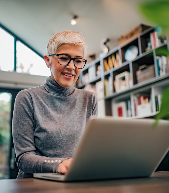 Frau sitzt am Schreibtisch und arbeitet an ihrem Laptop