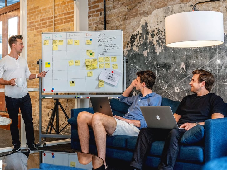 Two male colleagues sitting on sofa looking at flip chart and male colleague standing next to it 