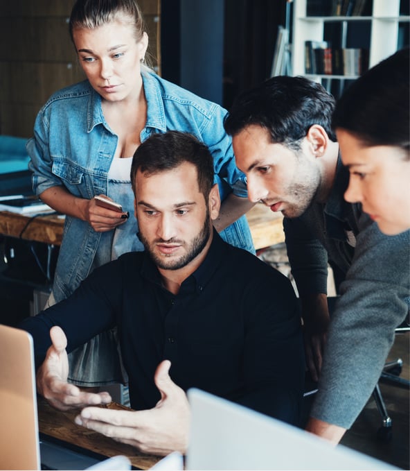 Vier Arbeitskollegen sitzen um einen Besprechungstisch und diskutieren, auf dem Tisch liegen Laptops