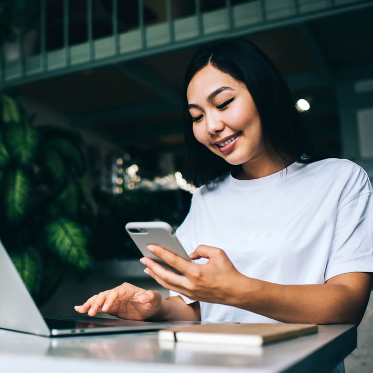 Woman sitting at desk typing on laptop with right hand and holding smartphone in left hand 