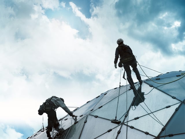 Two people secured with ropes climbing up glass roof 