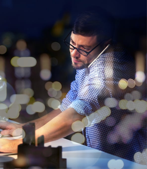 Man typing on keyboard and talking on phone at the same time with smartphone wedged between ear and shoulder 