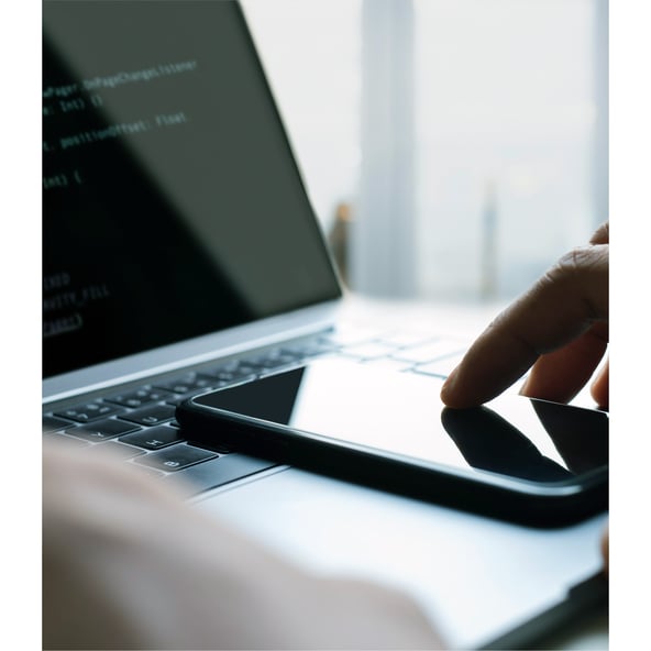 Hand touching smartphone lying on laptop keyboard 