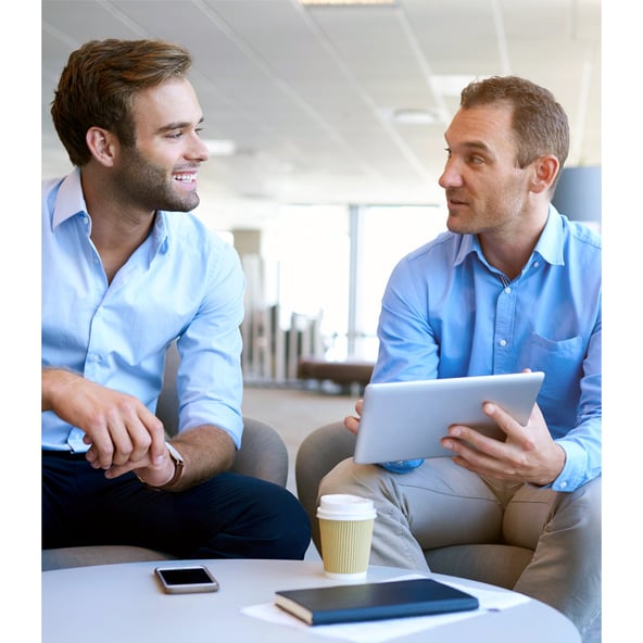 Male working colleague showing another working colleague wo is drinking coffee something on his tablet 