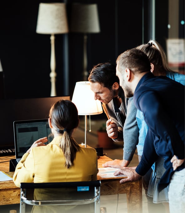 Female colleague shows something to three standing colleagues on her laptop 