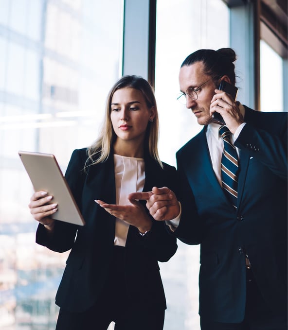 Female working colleague showing tablet to male working colleague on her right talking on the phone 