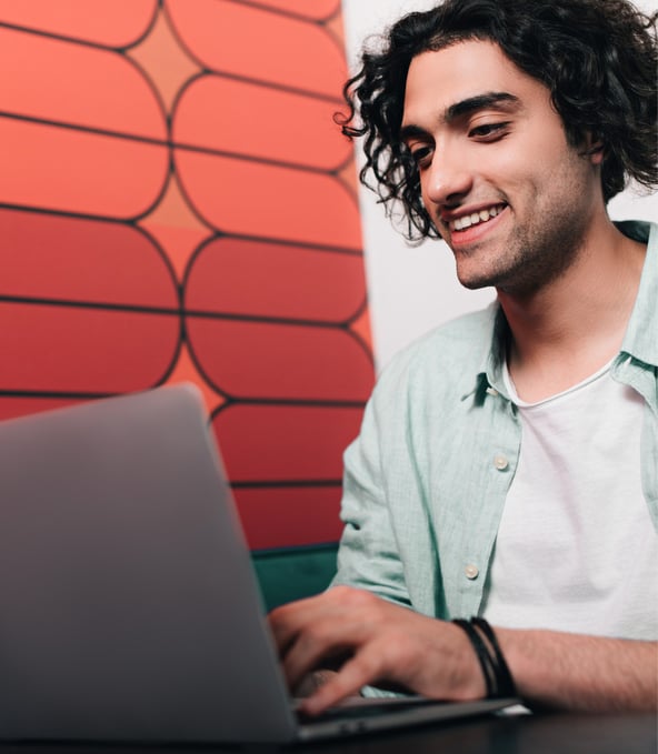 Mann sitzt hinter Laptop und lächelt 