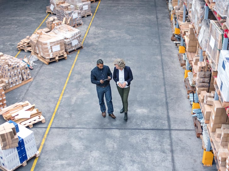 Two men with helmets walking through storehouse talking