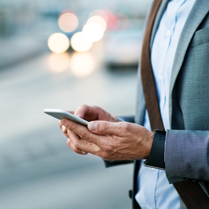 Mann im Anzug schaut auf sein Smartphone vor einem Gebäude 