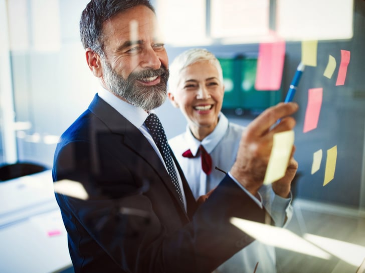 Female and male working colleagues smiling pointing at post-it on blackboard 