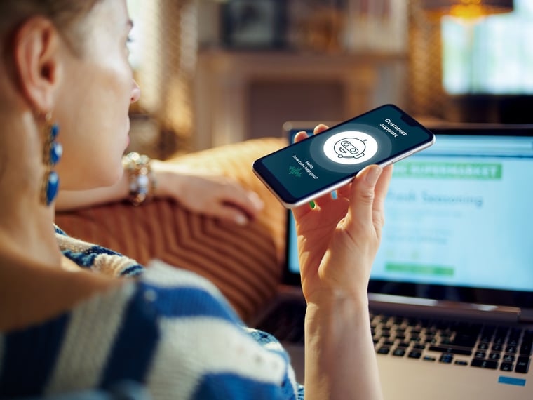 Woman holding smartphone in front of her and talking to Voicebot seen from behind 