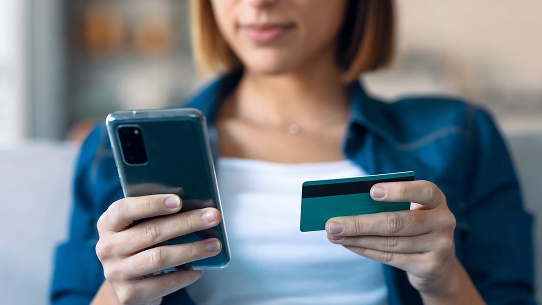 Woman looking at smartphone in her right hand and holding credit card in her left hand 