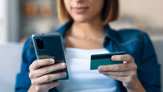 Frau blickt auf Smartphone in rechter Hand und hält Kreditkarte in linker Hand 