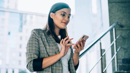 Woman standing on stairs in front of window typing on smartphone 
