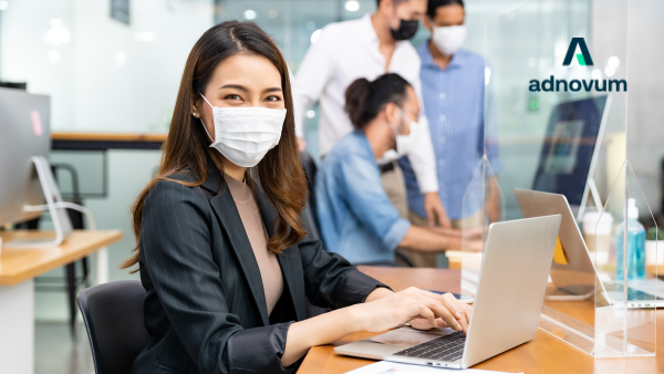 Several working colleagues in office, wearing masks and working on computers 