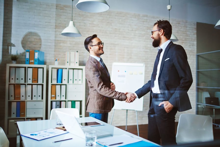 Two men shaking hands in office, one of them carrying briefcase 