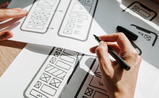 hand holding a pen and drawing mobile phone app layout designs