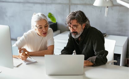 two people looking at a computer screen and taking notes