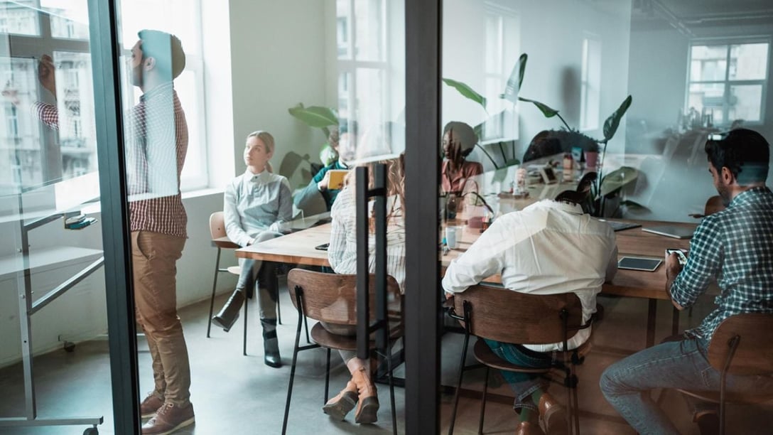 Three people in meeting room seen from behind through glass wall 