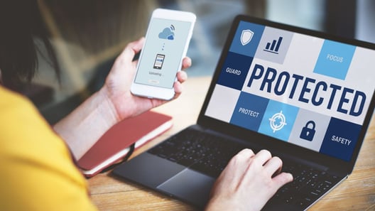 Woman looking at smartphone and typing on laptop which shows a page saying “protected” 