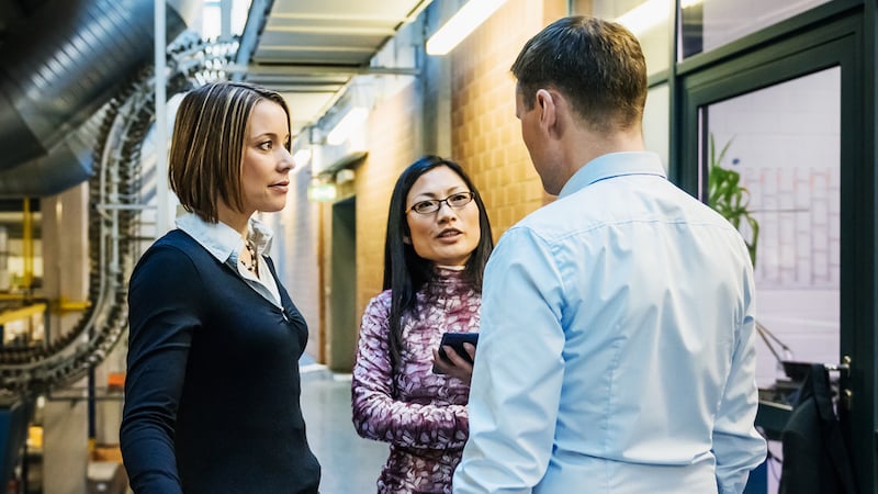 Two female and one male working colleague stand together in server room, talking 