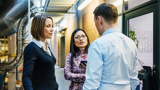 Two female and one male working colleague stand together in server room, talking 