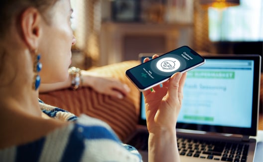 Frau hält Smartphone vor sich und spricht mit Voicebot von hinten gesehen 