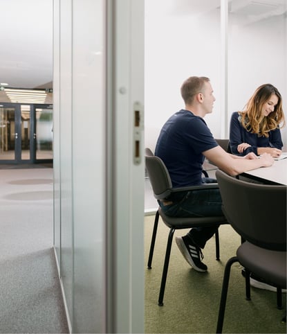 Female and male working colleagues sitting at desk in meeting room with open door  