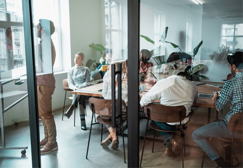 five people in meeting room seen from behind through glass wall 