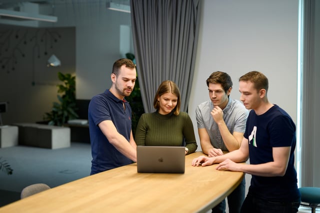 Four work colleagues sit around a meeting table and discuss, laptops 
