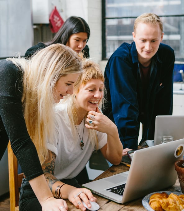 Drei weibliche und ein männlicher Arbeitskollege schauen lächelnd auf einen Laptop-Bildschirm 