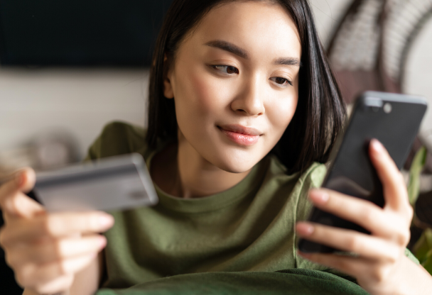 A young woman is using her credit card for online transactions on her phone