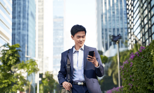 A male dressed in suit, holding on to a mobile phone with buildings in the background.