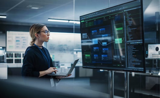 young_woman_holding_a_laptop_computer_and_looking_at_a_big_screen