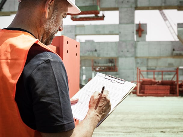 An engineer at a construction site writing on a clipboard