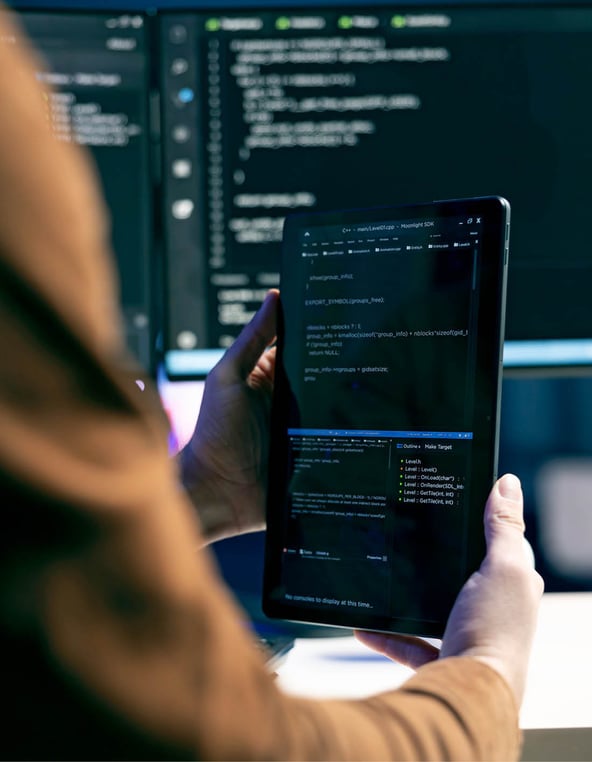 Person holding a tablet displaying code, with computer monitors in the background.